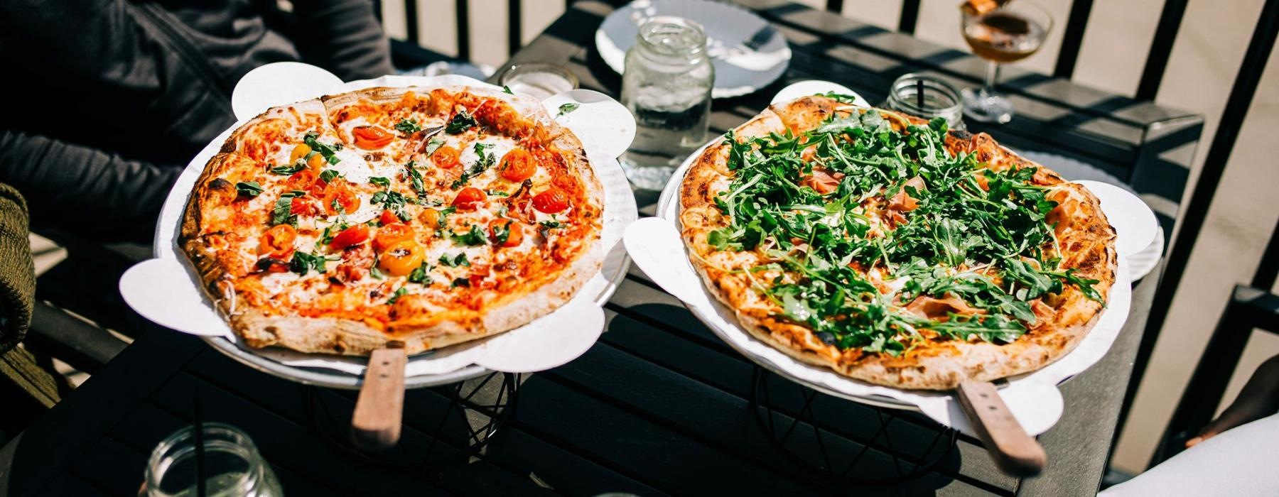 Two people with pizzas at a table outside